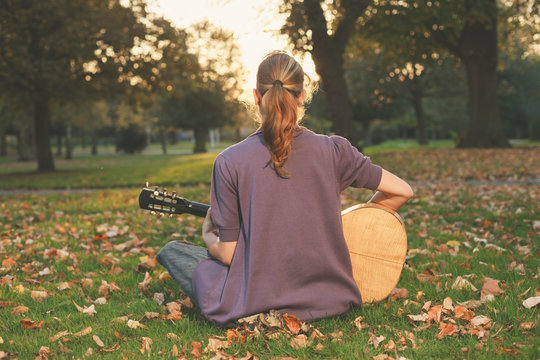 Woman playing guitar at sunset in the park