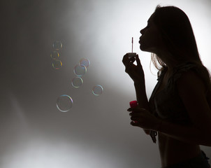 Girl blow bubbles on gray background.