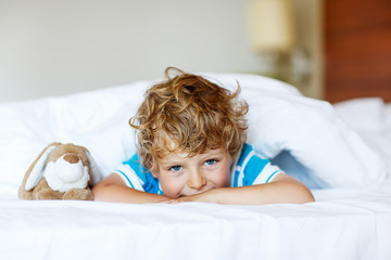 Adorable kid boy after sleeping in his white bed with toy