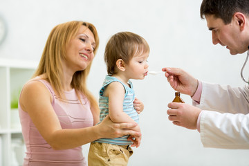 Doctor giving spoon dose of medicine drinking syrup to child