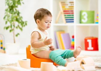 smiling baby sitting on chamber pot with toilet paper