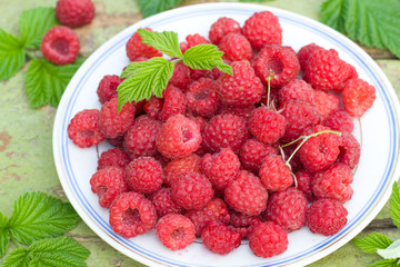 Fresh raspberries on a plate on old wooden table.