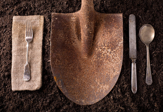 Rusted shovel on soil background with fork, knife, spoon, and na