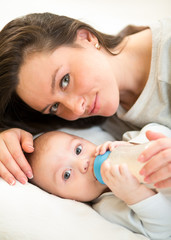 cute mother at home feeding baby son with a milk bottle