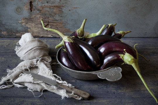 group of long eggplants on plate on wooden table with cloth