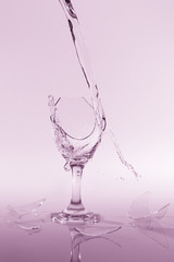 Clear water spill from a broken wine glass on colour background