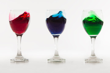 Three wine glasses with colour water spill on white background w
