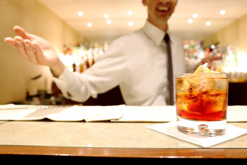 red cocktail over counter bar woth barman in the background