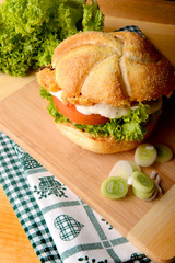 Appetizing fish burger in corn bun with leek on wooden board © jeliva