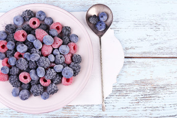 Iced berries on plate, on color wooden background