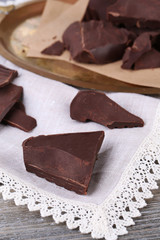 Cracked chocolate block on tray, on wooden background
