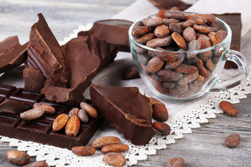 Cracked chocolate bar and cocoa beans on wooden background