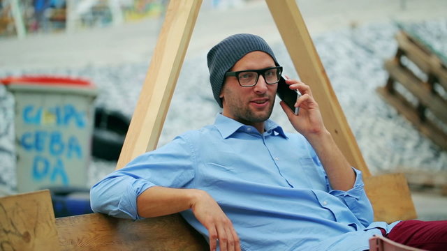 Man on wooden bech chatting on cellphone, steadycam shot