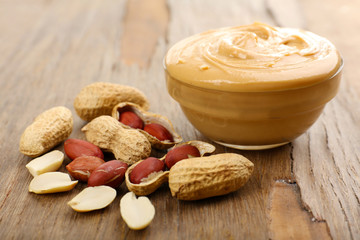 Creamy peanut butter in bowl on wooden table, close-up