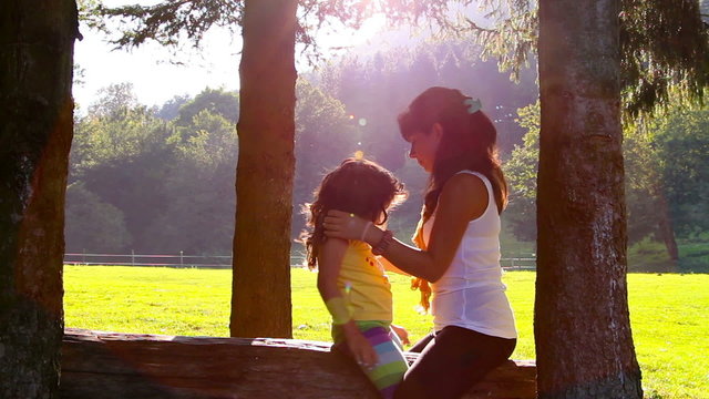 Mother and daughter hugging and kissing on tree log in Sunset
