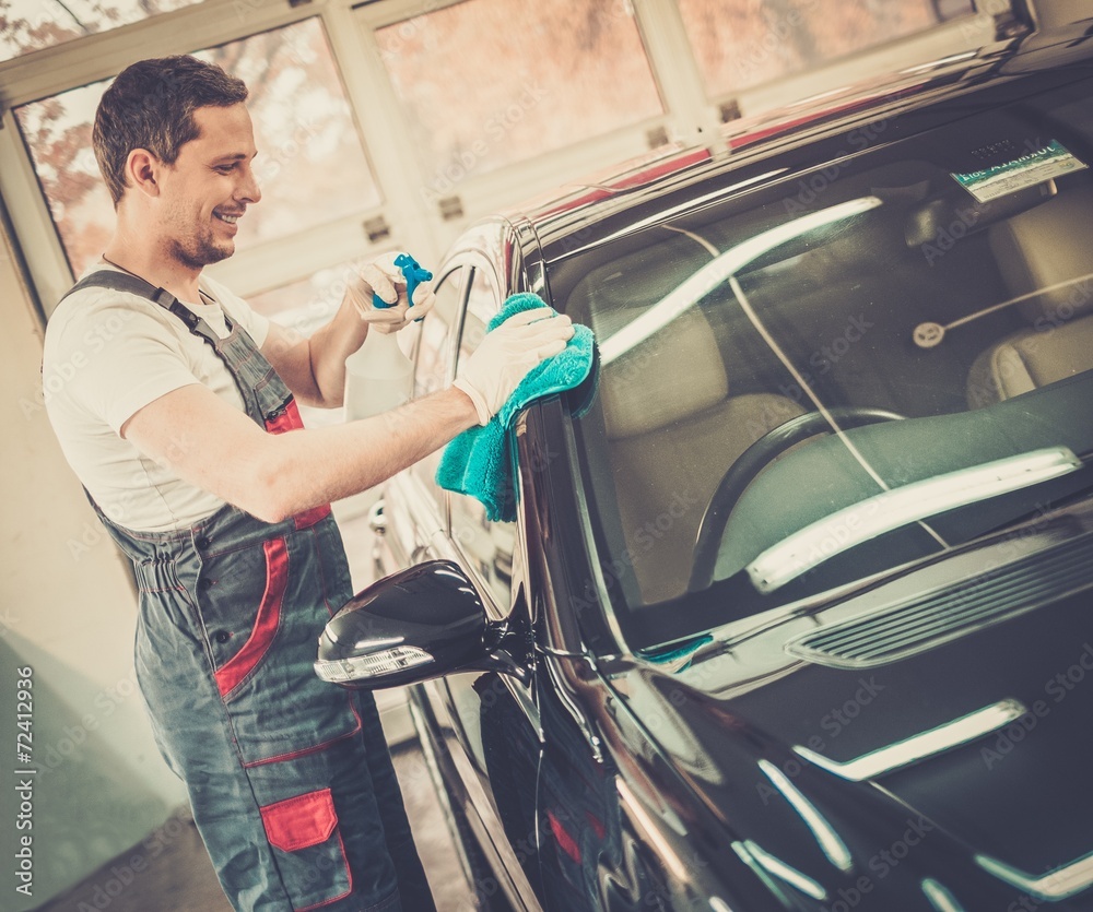 Wall mural Worker on a car wash cleaning car with a spray