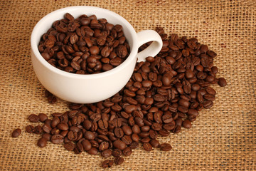 Coffee beans in white cup on brown sack background