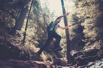 Man hiker jumping across stream in mountain forest