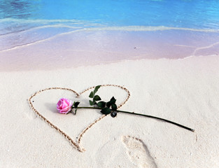 On a beach heart is drawn and the rose lies