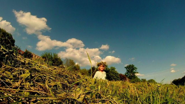 ittle girl weaves a wreath of grass on the field