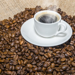 cup of coffee with a smoke and roasted coffee beans on burlap