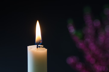 One burning candle at blurred heather