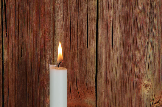 One burning candle at an old red wall