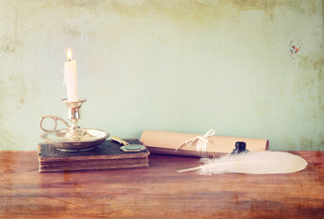 low key image of white Feather, inkwell and candle on old wooden