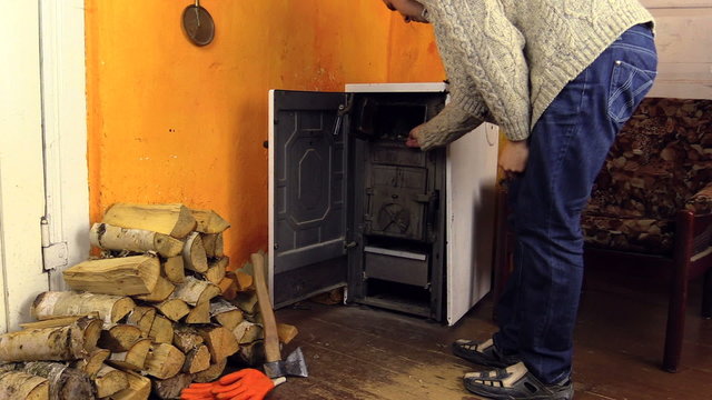 Villager man in sweater light firewood in stove with match