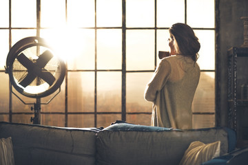 Young woman enjoying cup of coffee in loft apartment. rear view