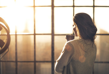 Young woman enjoying cup of coffee in loft apartment. rear view