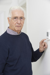 Worried Senior Man Turning Down Central Heating Thermostat