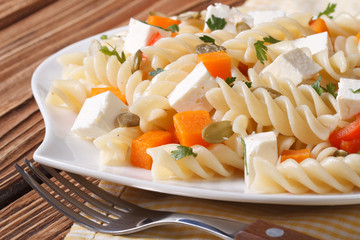 Pasta with pumpkin, feta and seeds on a white plate
