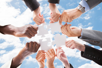 Multiethnic Business People Assembling Jigsaw Puzzle Against Sky
