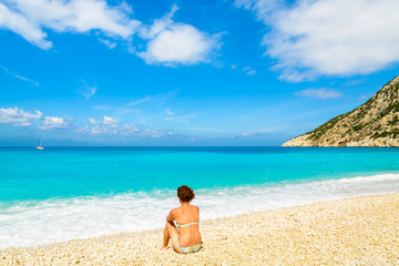 Fototapeta na wymiar Young woman sitting on beautiful Myrtos beach on Kefalonia islan