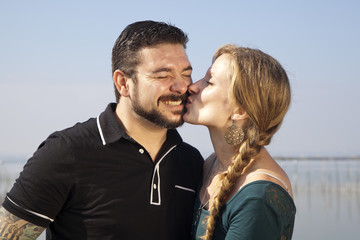 Mujer rubia con trenza besando a hombre con barba