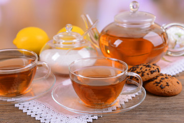 Teapot and cups of tea on table on light background