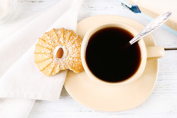 Cup of coffee with tasty cookie on color wooden background