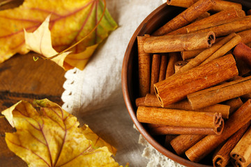 Cinnamon sticks in bowl with yellow leaves on wooden background
