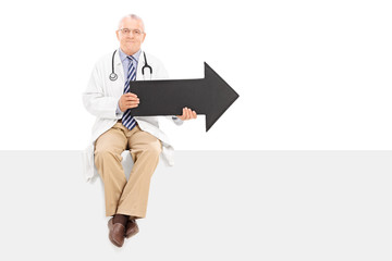 Mature doctor holding an arrow and sitting on a panel