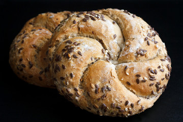 Whole wheat kaiser rolls with sesame seeds on black surface.