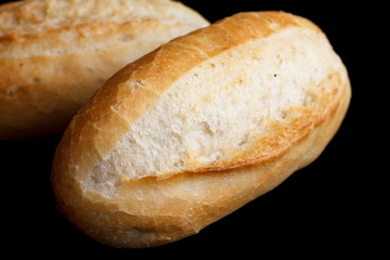 Whole white mini baguettes on black background.