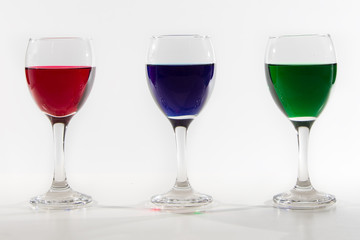 Three wine glasses with colour water spill on white background w