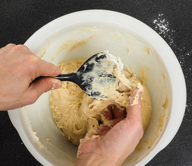 Person handling a sticky dough with black spatula in white plast