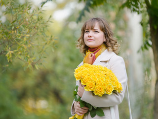 Girl on nature with a bouquet of yellow roses
