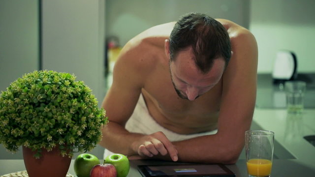 Man after shower watching photos on tablet in the kitchen 