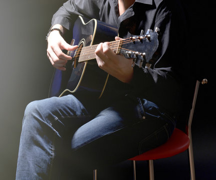 Young musician playing acoustic guitar on dark background