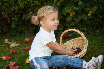 Mädchen sammelt Kastanien in einem Korb und freut sich