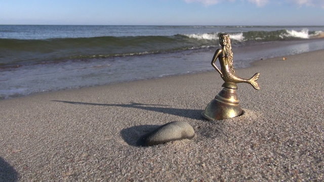 brass bell with mermaid figure sculpture on sea beach
