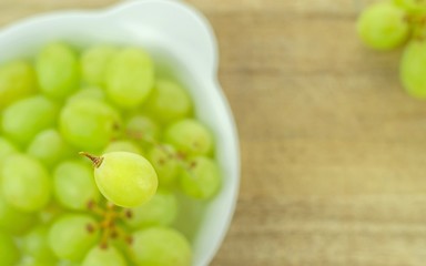 Selective focus of a single grape over a bowl of grapes